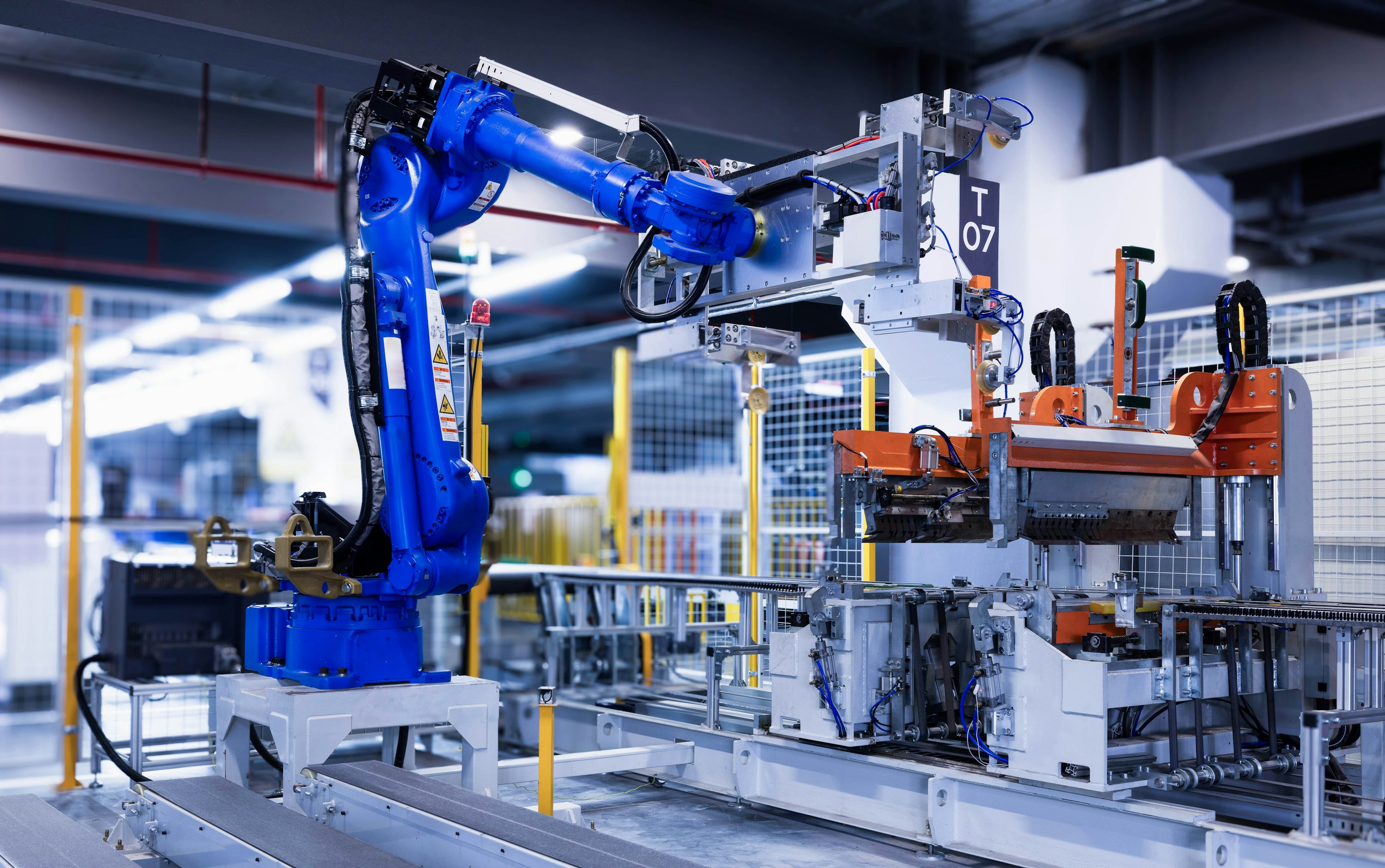 Blue industrial robot arm with handling fixtures and a conveyor in a factory