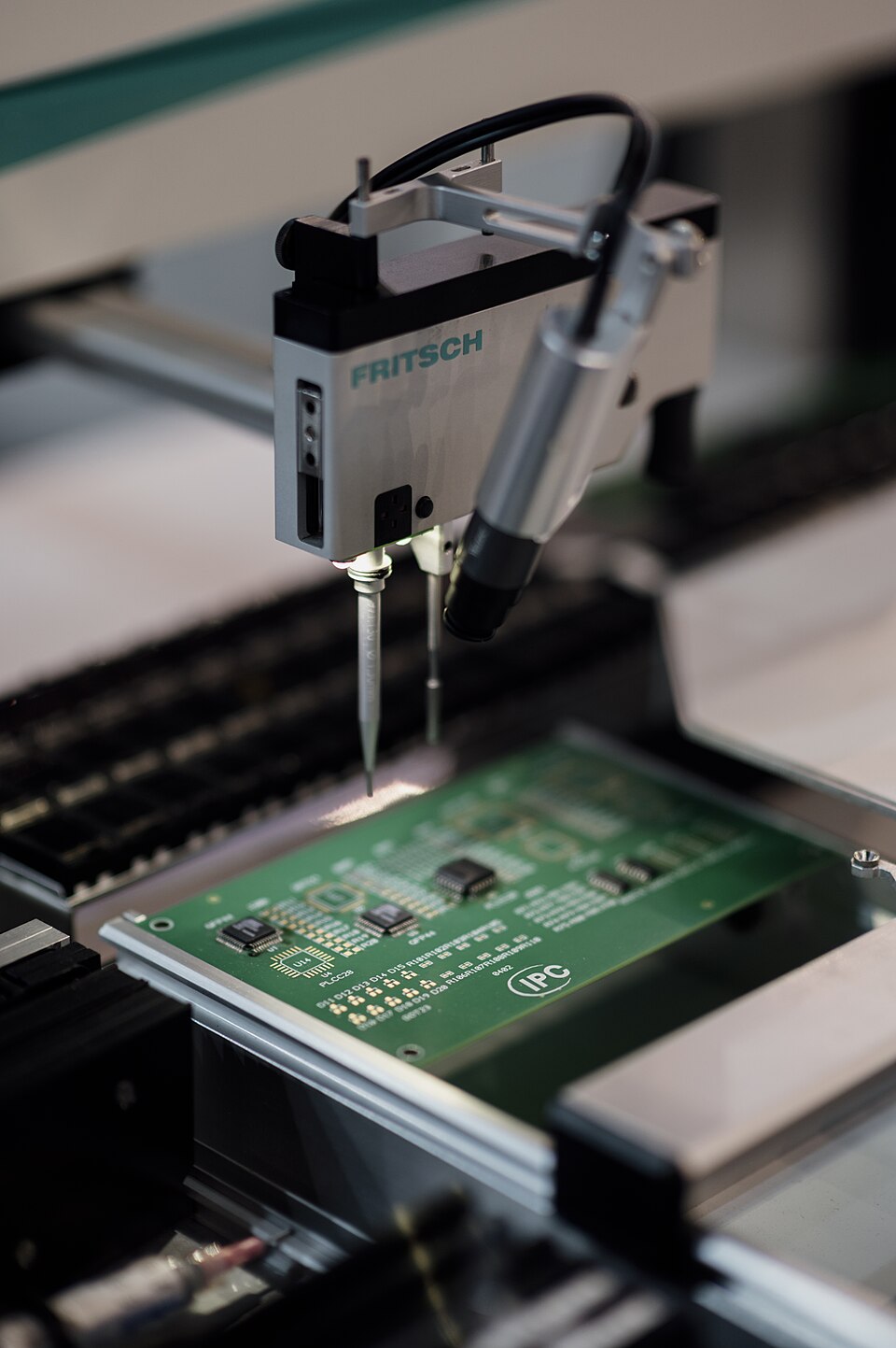 A component-placement head above a green circuit board inside an electronics assembly machine, with no people in the photograph.
